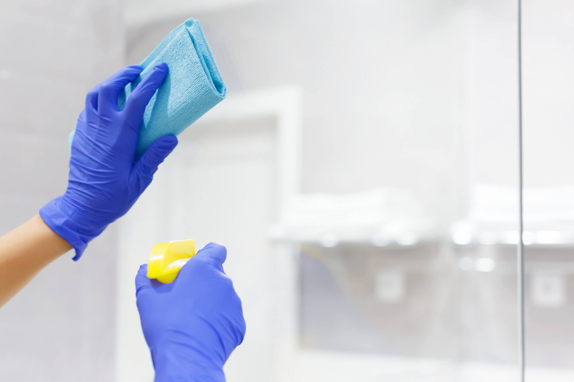 Zwei H&auml;nde mit Putzhandschuhen, Schwamm und Spr&uuml;hflasche bei der Fensterreinigung